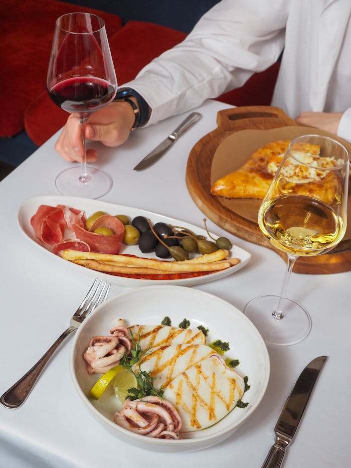 Elegant table setting with wine, antipasto platter, and gourmet pizza, perfect for fine dining.