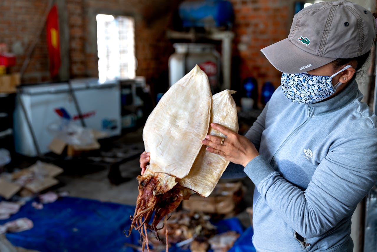 A woman in a face mask holds a dried squid at an indoor seafood market.